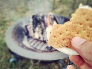 hand holding s'more in front of a fire on a firepit grill