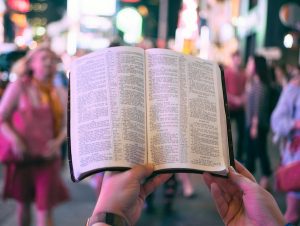 Bible being held by two hands up in air, in the midst of a crowd