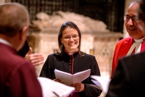 a shorter woman with glasses, smiling, standing in a circle with several male colleagues, all dressed in various church vestments