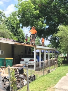 adult man in hat and teenagers on the roof of a one-story house with trees overhead