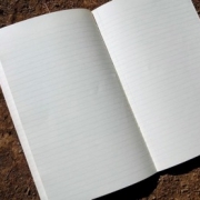 A lined paper notebook sitting open to blank pages on top of some soil.
