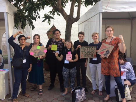 7 people standing holding signs supporting protecting transgender youth, 1 person kneeling