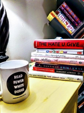 mug reading "read fewer white dudes" on it on a shelf next to a pile of books by non-white authors