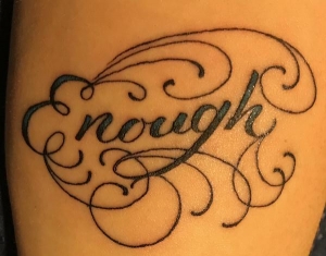 a black-ink tattoo of the word "enough" with curlicue decorations around it